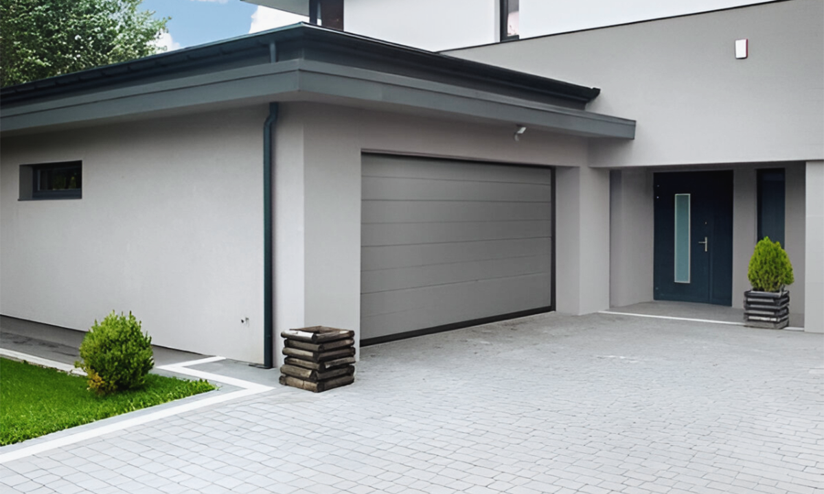 Modern villagarageport i grått, monterad i en stilren fasad med stensatt infart.