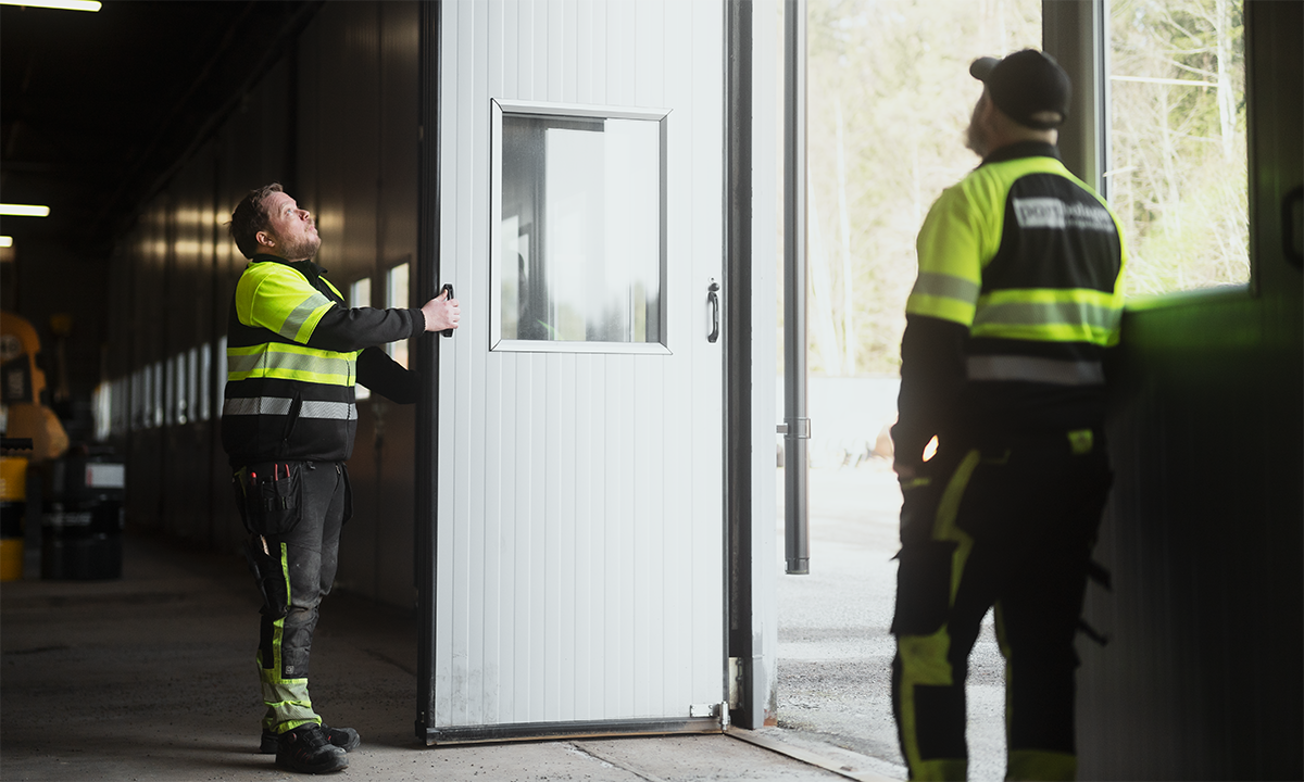 Två medarbetare från Portbolaget i Bergslagen öppnar en vit vikport i industrimiljö.