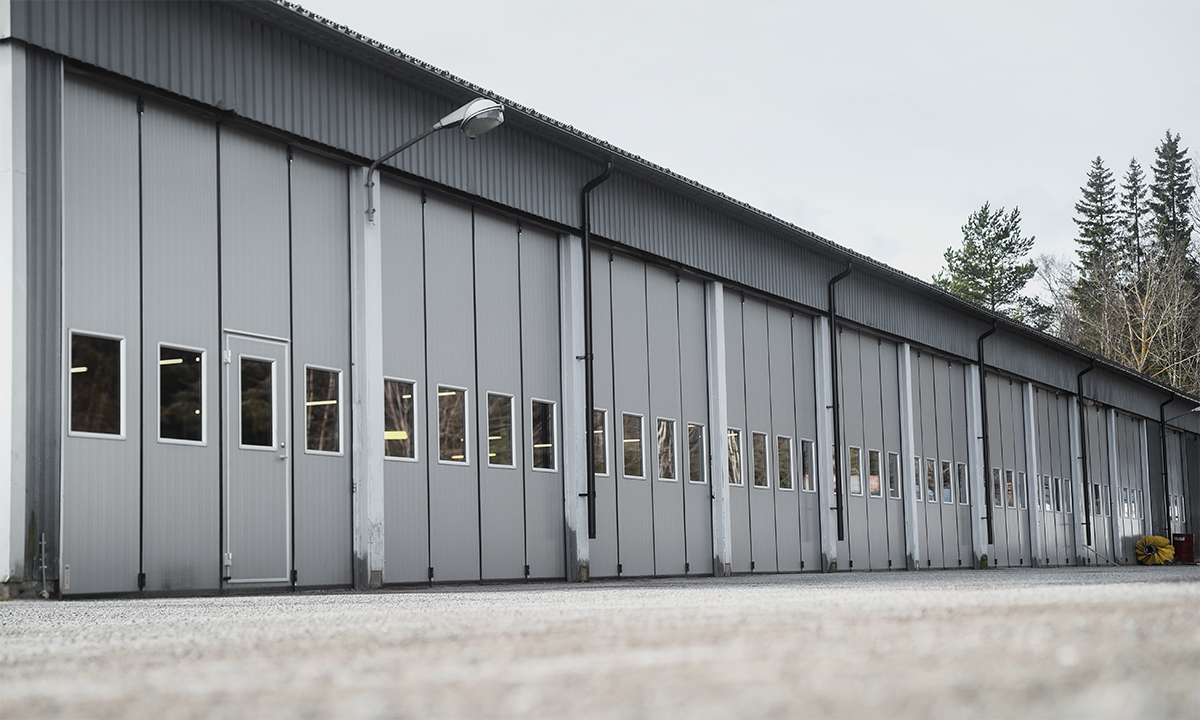 Lång industribyggnad med flera vikportar i grått, utrustade med fönster för ljusinsläpp.